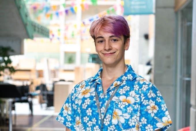 Felix with pink hair and wearing a blue shirt with white flowers.