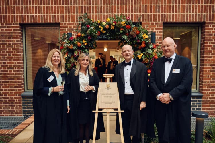 Four people standing by a flower arch at Norham St Edmund dressed in academic gowns