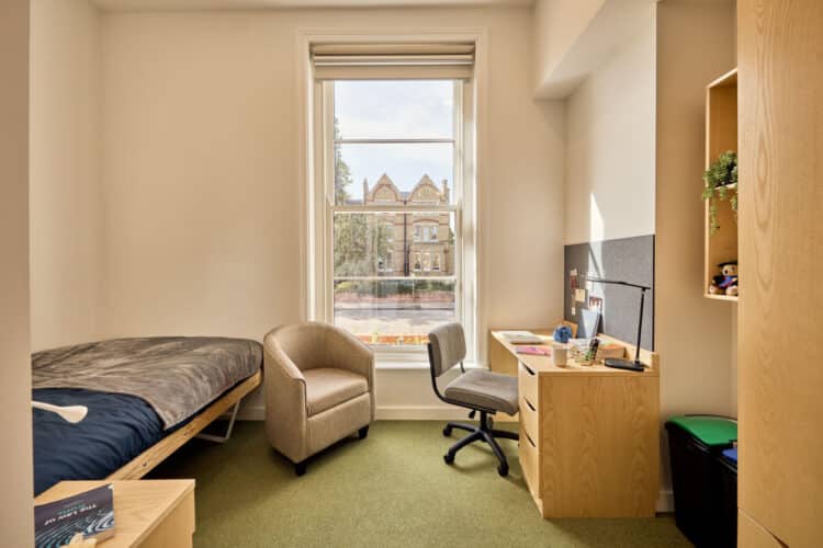 Student bedroom showing a bed, chair and desk with shelving looking out onto a window