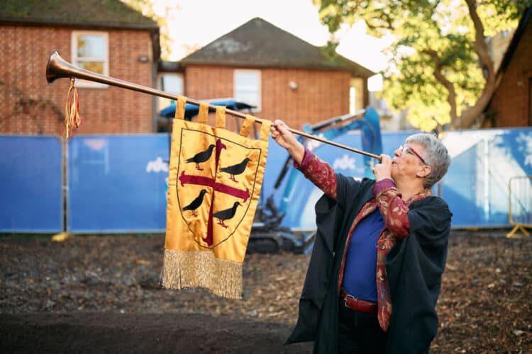 Hall Fellow Professor Henrike Lähnemann using the Hall's ceremonial trumpet to mark breaking ground.