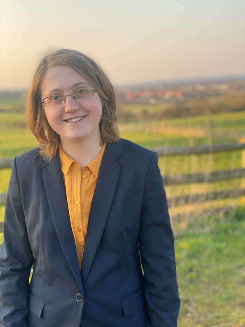 Isabel stands in a field, wearing a suit