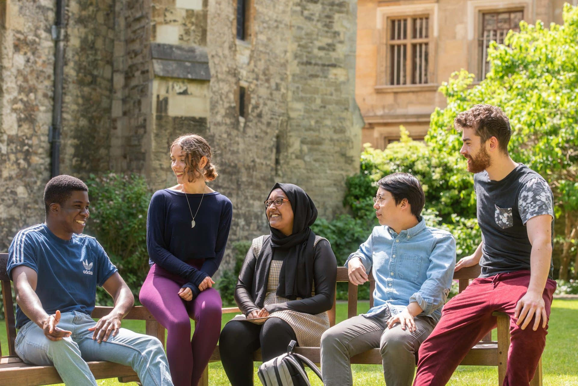 Students sitting on a bench in the Broadbent Garden behind the College Library