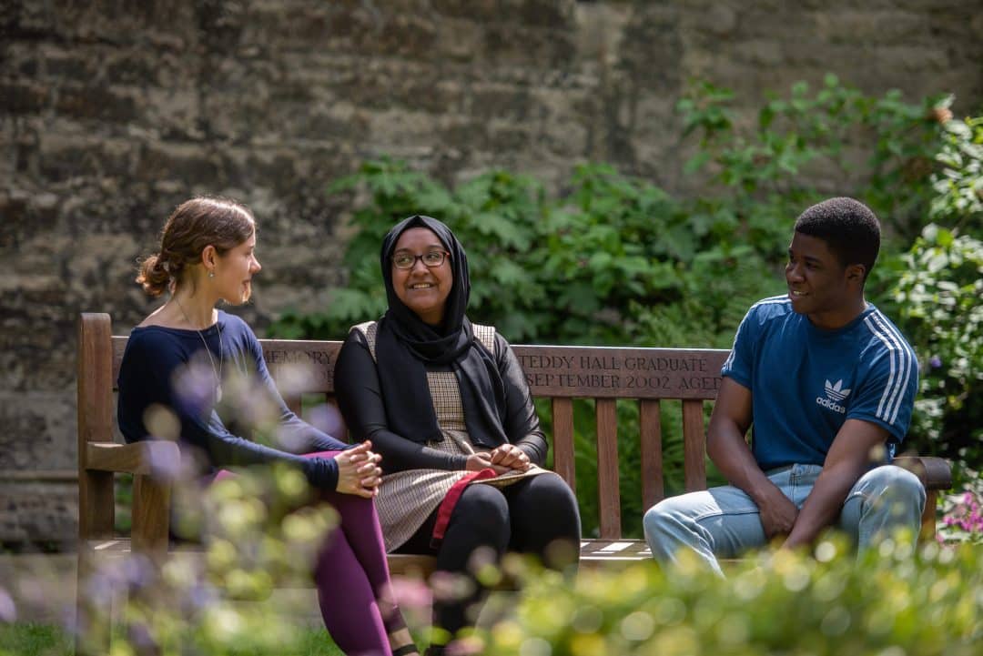 Students sitting on a bench in the Broadbent Garden behind the College Library