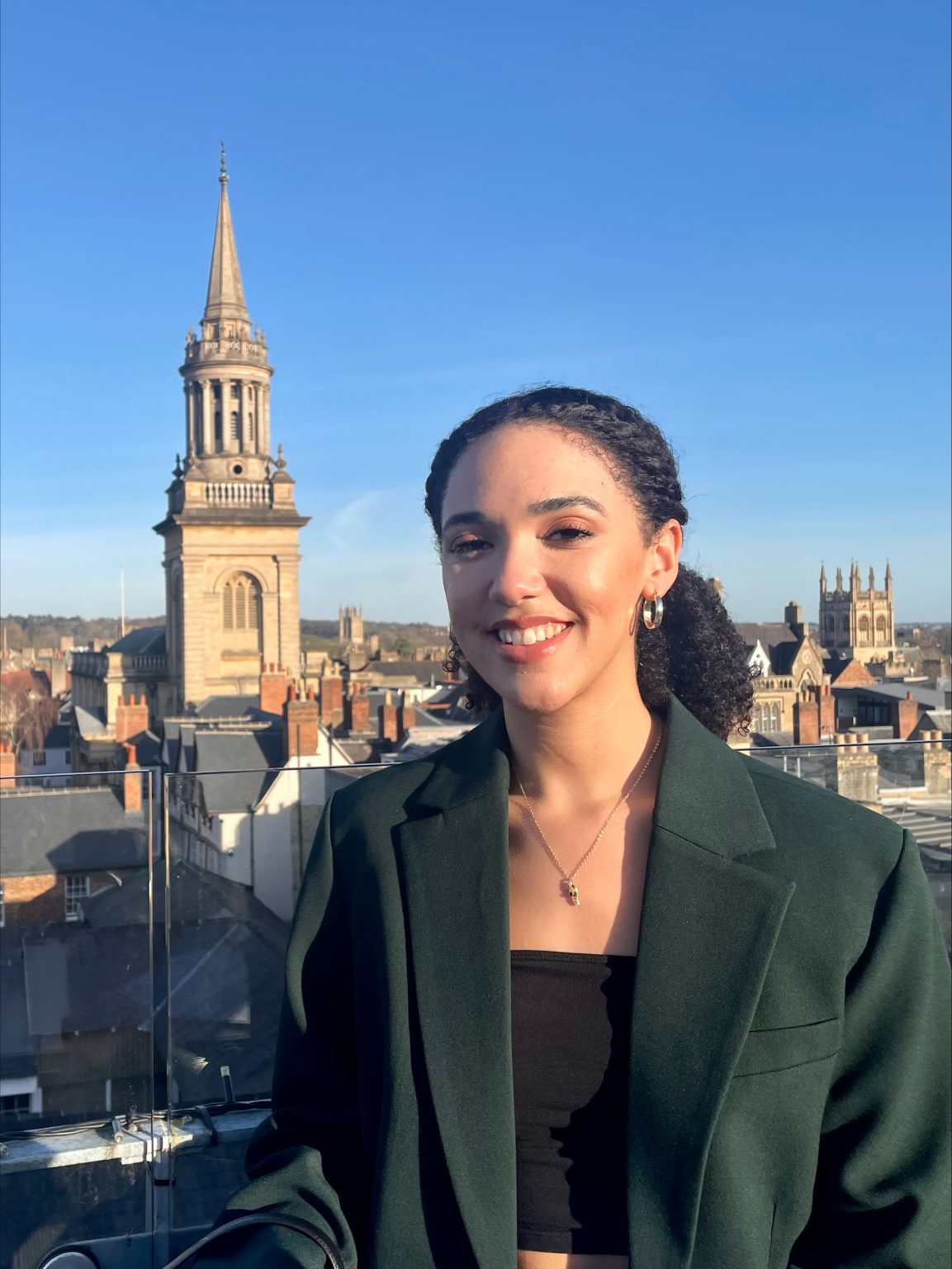 Zoe smiles at the camera, the Oxford skyline behind her