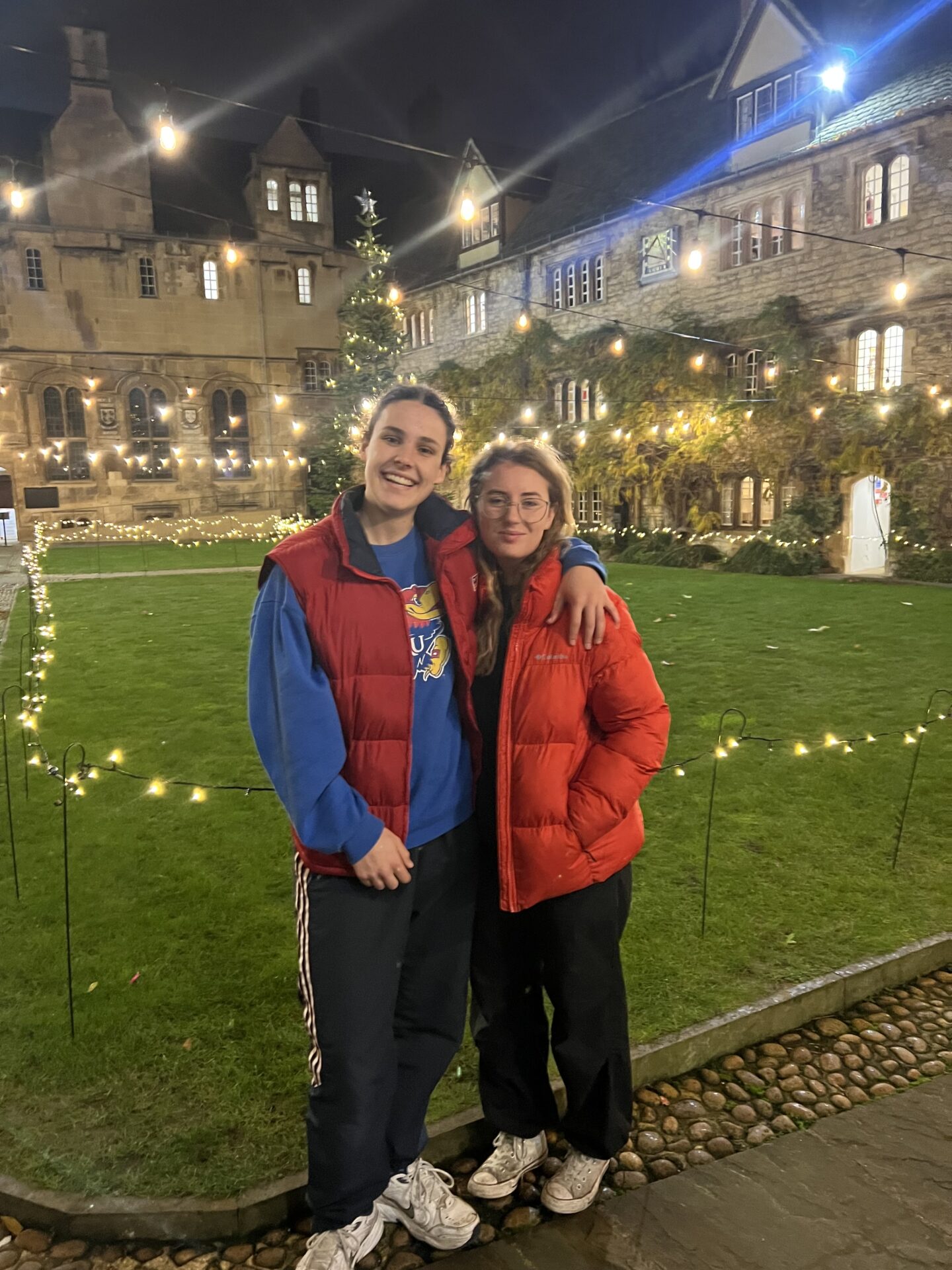 Harriet and Sarah stand in Front Quad at night, surrounded by the Christmas lights