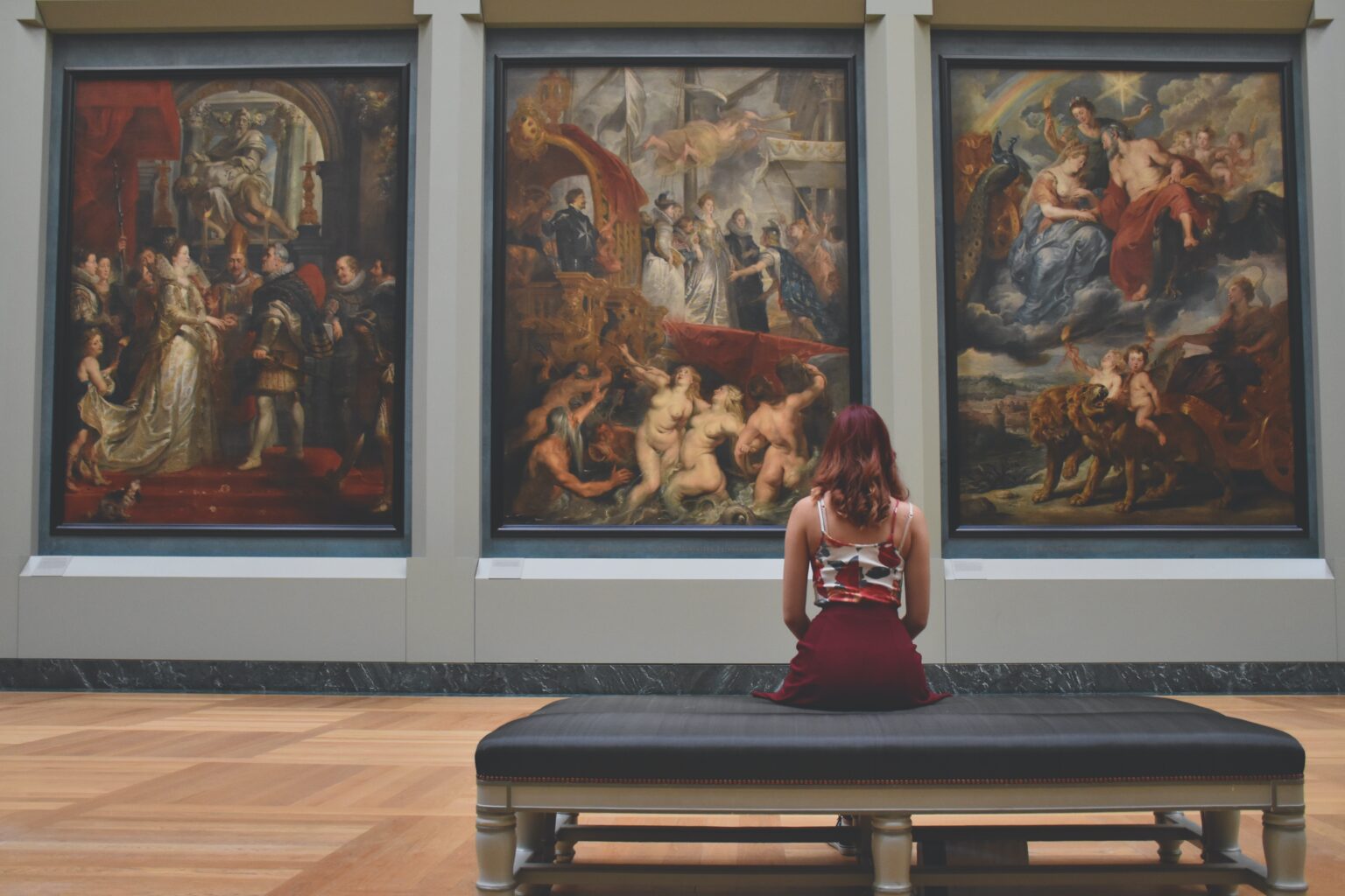 3 paintings in a gallery, a person sits in front of them