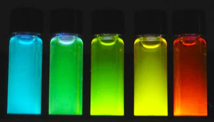 Five vials of liquid containing quantum dots which flouresce cyan, light green, green yellow and red under UV light